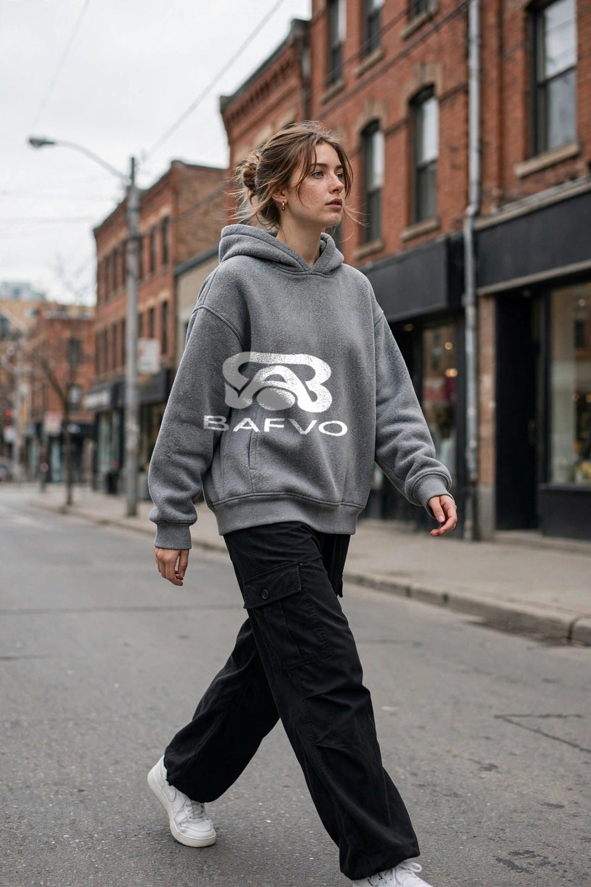Woman wearing a grey BAFVO hoodie walking on a Toronto street with brick storefronts