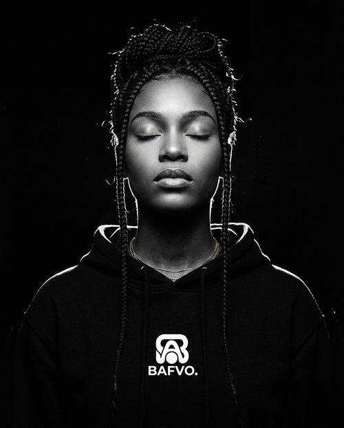 Portrait studio en noir et blanc d'une femme aux cheveux tressés portant un sweat à capuche BAFVO noir