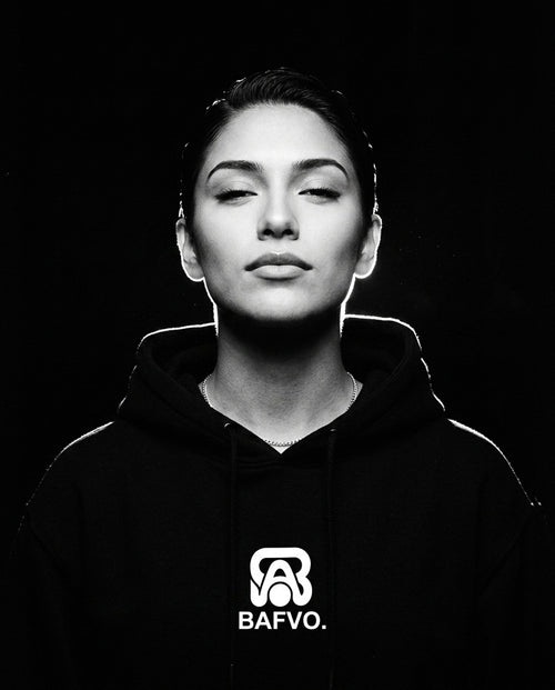 Portrait studio en noir et blanc d'une femme portant un sweat à capuche noir BAFVO avec logo sur la poitrine
